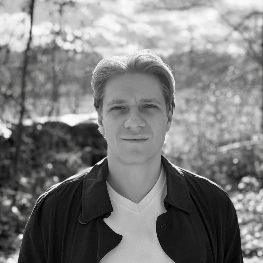 A person wearing a VR headset in a dark room lit with red and blue lights, smiling and reaching forward as if interacting with virtual objects.