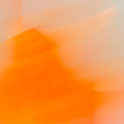 The bottle is positioned diagonally and appears to be balanced on a large, reflective, circular object . The scene is illuminated by warm, orange/amber light, and a fine mist of spray is visible near the top of the bottle.